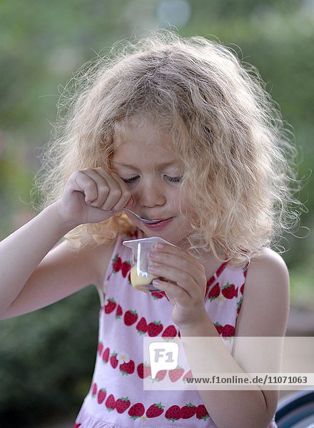 Young girl with blond curly hair  eating yogurt  Sweden  Europe