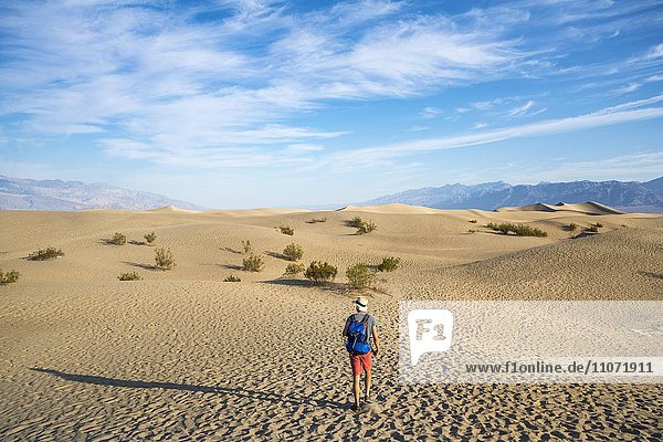 Junger Mann  Tourist wandert auf Sanddünen  Mesquite Flat Sand Dunes  hinten Ausläufer der Amargosa-Range Bergkette  Death Valley  Death-Valley-Nationalpark  Kalifornien  USA  Nordamerika