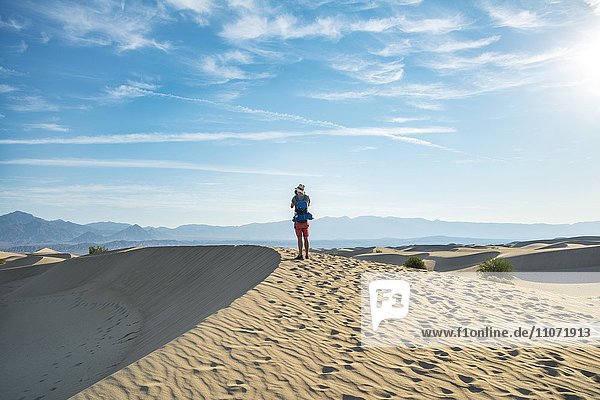 Junger Mann  Tourist fotografiert Sanddünen  Mesquite Flat Sand Dunes  hinten Ausläufer der Amargosa-Range Bergkette  Death Valley  Death-Valley-Nationalpark  Kalifornien  USA  Nordamerika