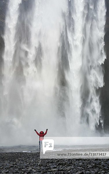 Wanderer mit ausgestreckten Armen vor Wasserfall Skogafoss im Winter Skógar Südisland Island Europa