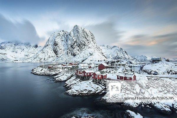 Ortsansicht  Rorbuer Fischerhütten vor verschneiten Bergen im Winter  Sakrisøya  Moskenesøy  Lofoten  Norwegen  Europa