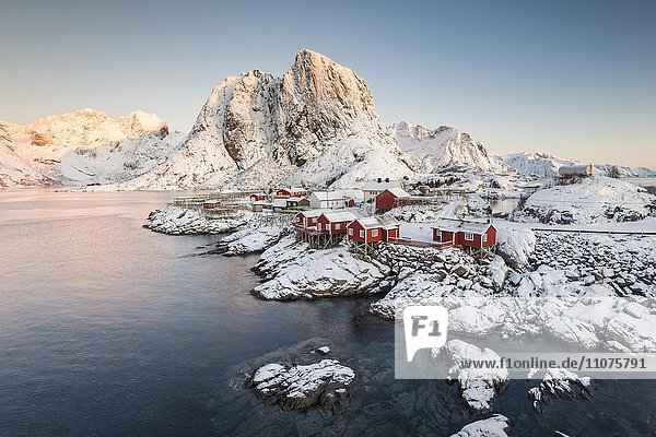 Ortsansicht  Rorbuer Fischerhütten vor verschneiten Bergen im Winter  Sakrisøya  Moskenesøy  Lofoten  Norwegen  Europa