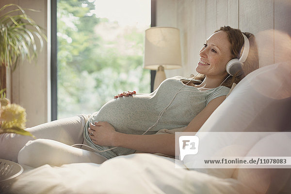 Lächelnde Schwangere entspannt Musik hören mit Kopfhörern im Bett