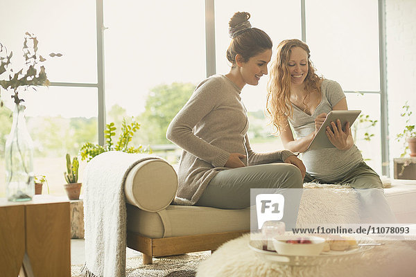 Schwangere Frauen mit digitalem Tablett im Wohnzimmer