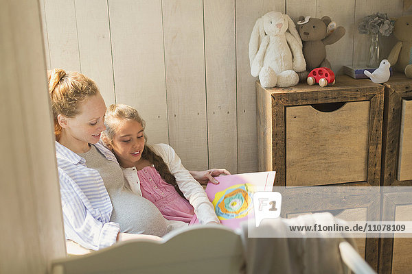 Schwangere Mutter und Tochter lesen Märchenbuch im Kinderzimmer