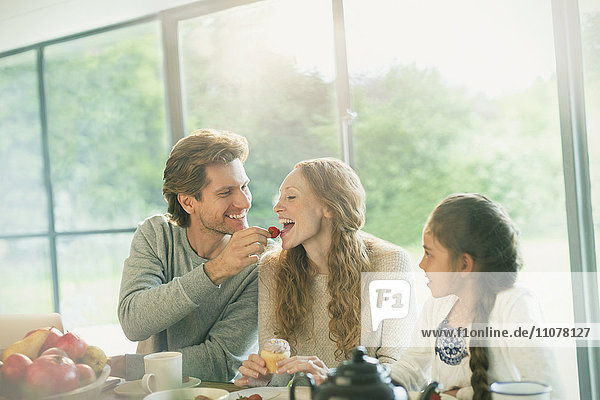 Husband feeding wife strawberry at table