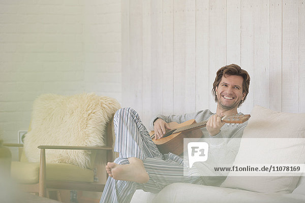 Smiling man in pajamas playing guitar in living room