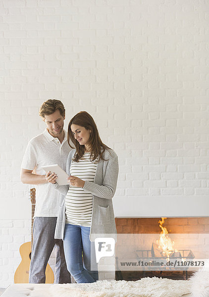 Schwangeres Paar mit digitalem Tablett in der Nähe des Kamins