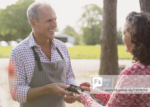 Lächelnde Pflanzengärtnerin  die dem Kunden eine Kreditkartenmaschine anbietet.