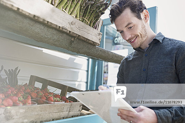 Lächelnder Bauernmarktarbeiter überprüft Inventar mit Zwischenablage neben Erdbeeren