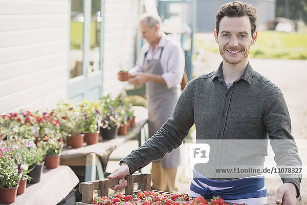 Portrait lächelnder Bauernmarktarbeiter mit Erdbeerkiste