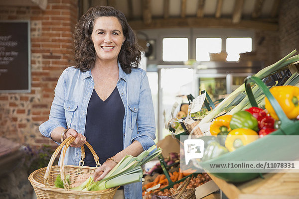 Portrait lächelnde Frau mit Einkaufskorb für Produkte auf dem Markt