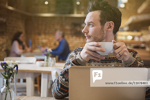 Nachdenklicher Mann beim Kaffeetrinken am Laptop im Cafe