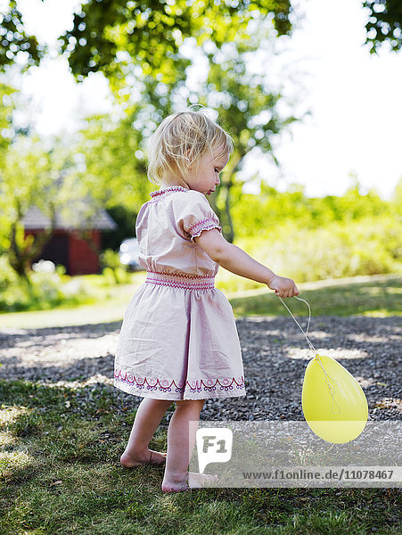 Ein Mädchen in einem rosa Kleid spielt mit einem Luftballon.