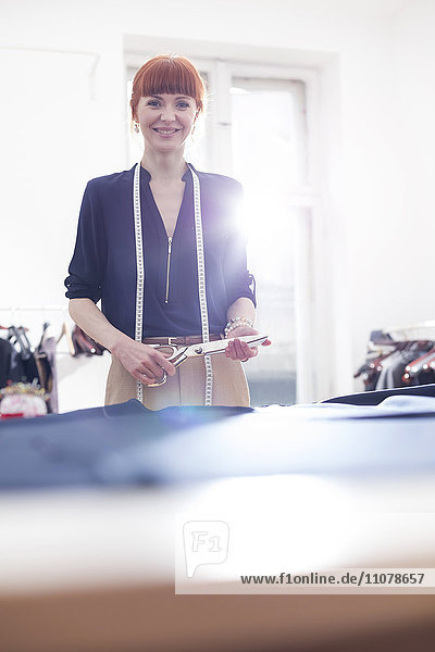 Portrait confident female tailor holding scissors in menswear workshop