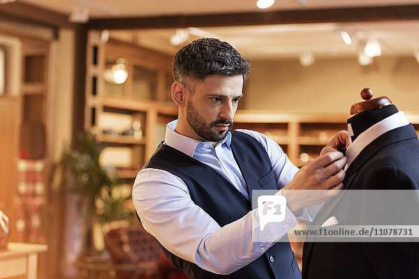 Tailor adjusting tie on dressmakers model in menswear shop