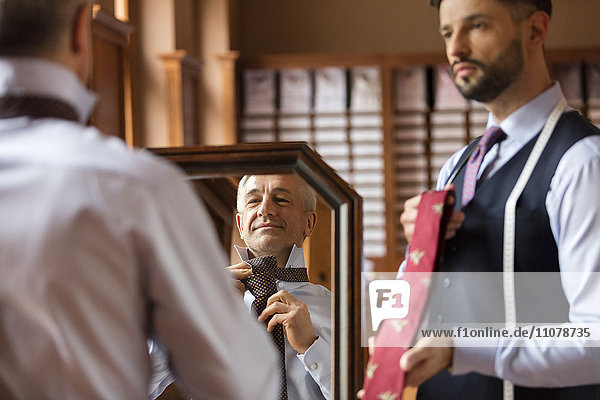 Tailor showing ties to businessman at mirror in menswear shop