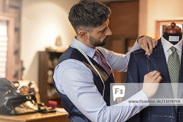Tailor adjusting suit on dressmakers model in menswear shop