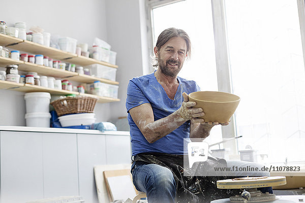 Porträt selbstbewusster reifer Mann hält Schale an Töpferscheibe im Atelier