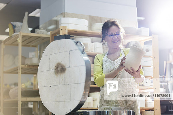 Lächelnde reife Frau stellt Keramikvase in den Ofen im Atelier