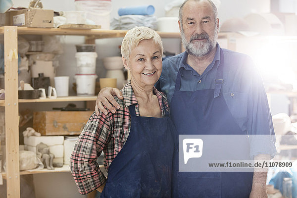 Portrait lächelndes Seniorenpaar mit Schürzen im Töpferatelier