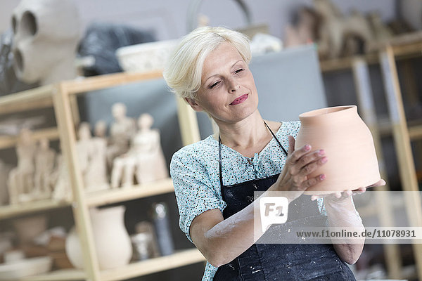 Mature woman holding pottery vase in studio