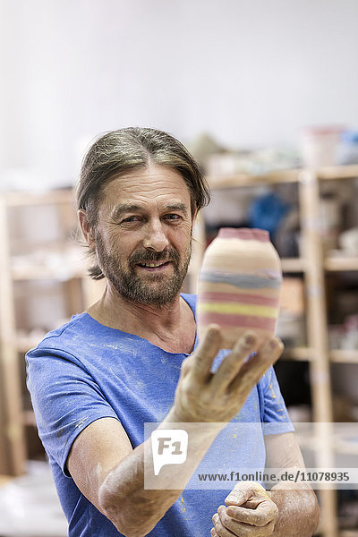 Portrait lächelnder reifer Mann mit bemalter Keramikvase im Atelier