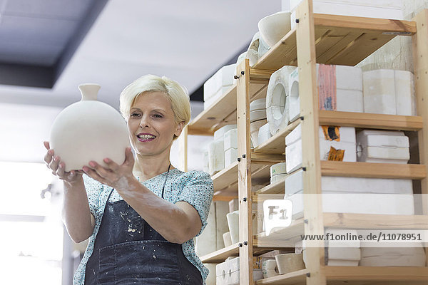 Smiling woman holding pottery vase in studio