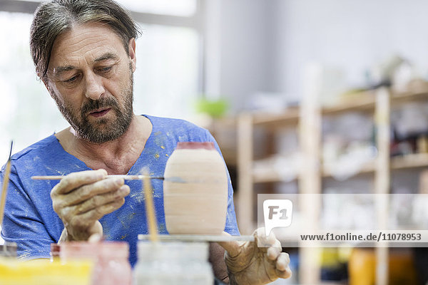 Fokussierter reifer Mann bemalt Keramikvase im Atelier