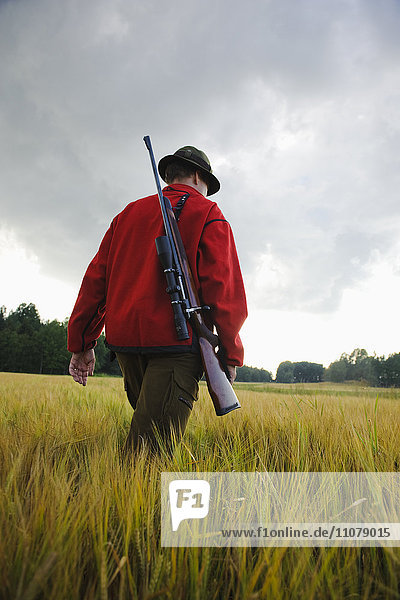 Man carrying rifle walking through field