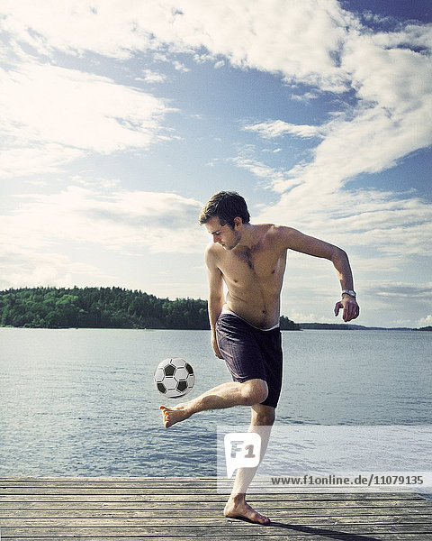 Junger Mann spielt mit Fußball auf dem Steg