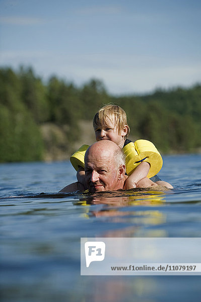 Großvater trägt Mädchen auf dem Rücken und schwimmt im See