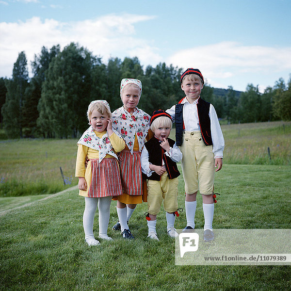 Children in traditional clothing standing on grass field portrait