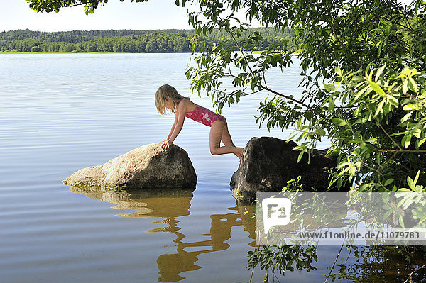Mädchen balanciert zwischen zwei Steinen im See