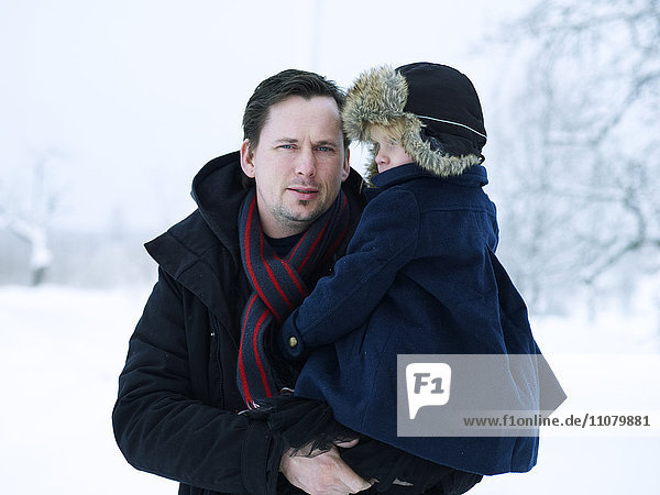 Portrait of father holding daughter in winter landscape