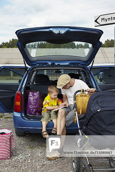 Vater mit Sohn liest im Kofferraum eines Autos