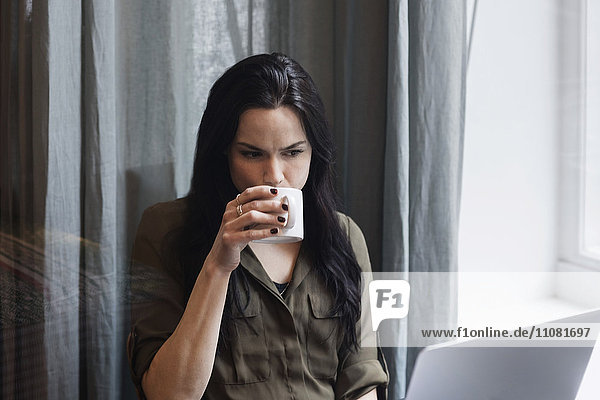 Female blogger drinking coffee while working in creative office
