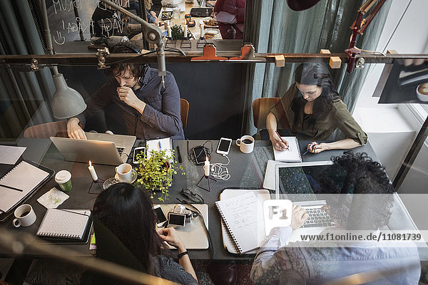 Hoher Blickwinkel auf das kreative Team  das am Tisch im Büro arbeitet  durch Glas gesehen