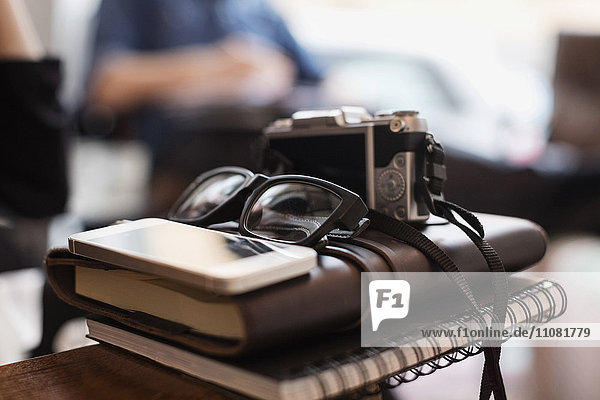 Nahaufnahme von Kamera und Brille mit Smartphone auf Tagebüchern im Kreativbüro