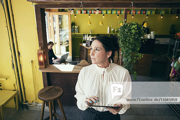 High angle view of female owner holding digital tablet while looking away in cafe