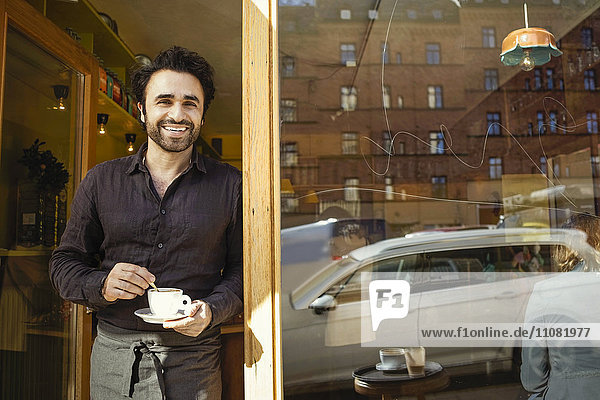 Porträt eines glücklichen Barista mit Kaffeetasse vor der Tür
