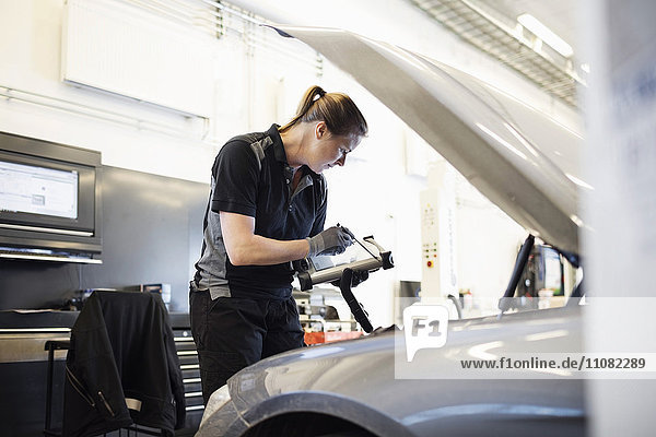 Mechanikerin mit Technik bei der Untersuchung des Autos in der Werkstatt