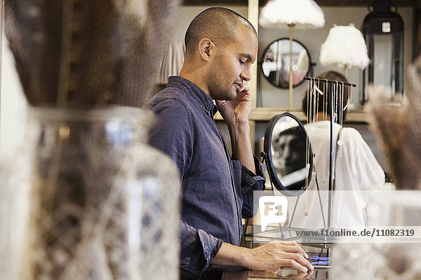 Seitenansicht des männlichen Besitzers  der am Telefon spricht  während er im Laden steht.