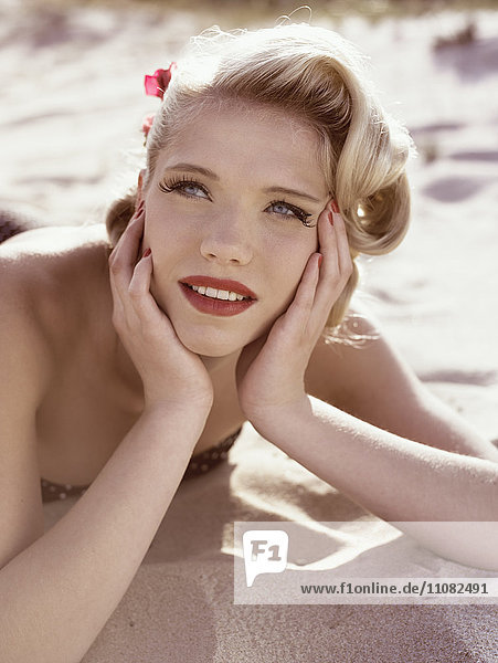 Porträt einer jungen Frau mit Retro-Frisur  die auf Sand liegt
