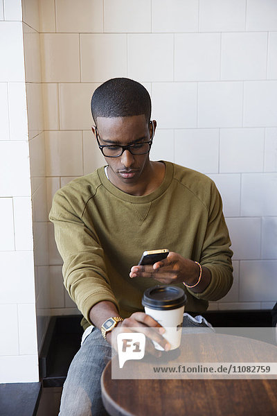 Junger Mann im Café mit Mobiltelefon