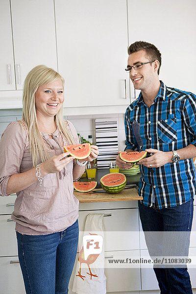 Young happy couple in kitchen eating watermelon
