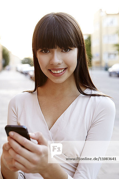 Porträt einer lächelnden jungen Frau  die ein Mobiltelefon benutzt  Stockholm  Schweden