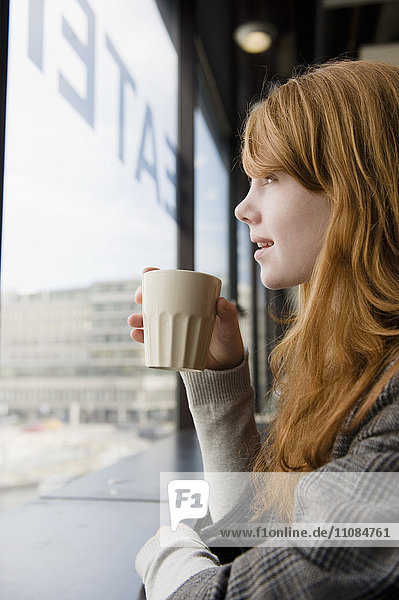 Junge Frau trinkt Kaffee und schaut durch das Fenster