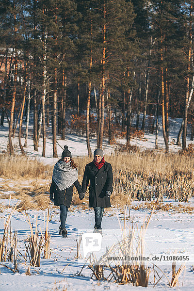 Young couple holding hands while walking on snow covered field