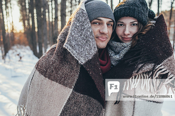 Porträt eines lächelnden Paares in Decke gehüllt  während es auf einem schneebedeckten Feld steht.